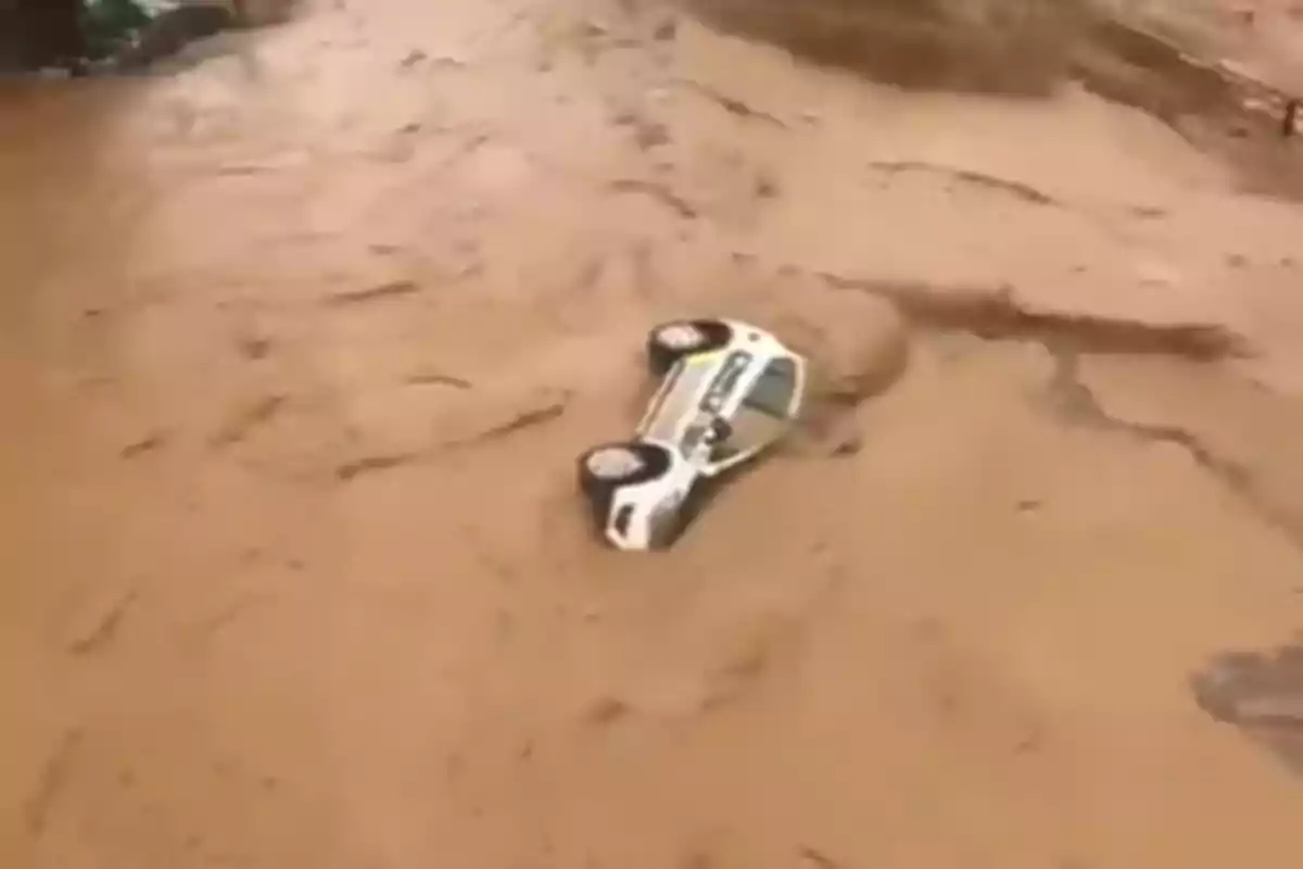 Un coche volcado parcialmente sumergido en un río de lodo durante una inundación.