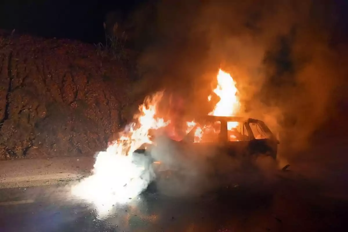 Un coche en llamas en una carretera durante la noche.