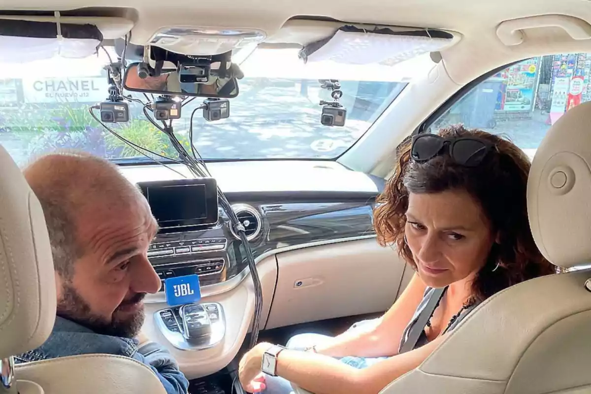 Dues persones assegudes als seients davanters d'un automòbil amb diverses càmeres muntades al parabrisa. Dues persones assegudes als seients davanters d'un automòbil amb diverses càmeres muntades al parabrisa.
