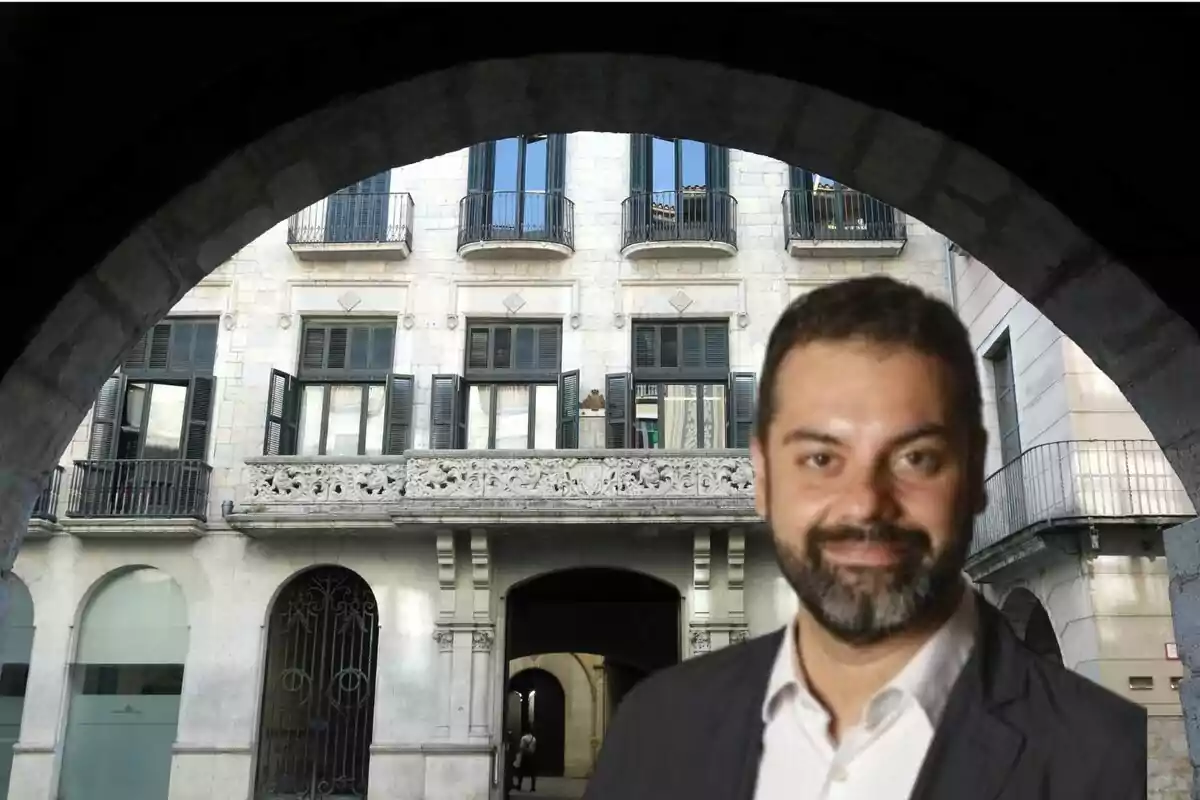 Hombre con barba y traje frente a un edificio histórico con balcones y arcos.