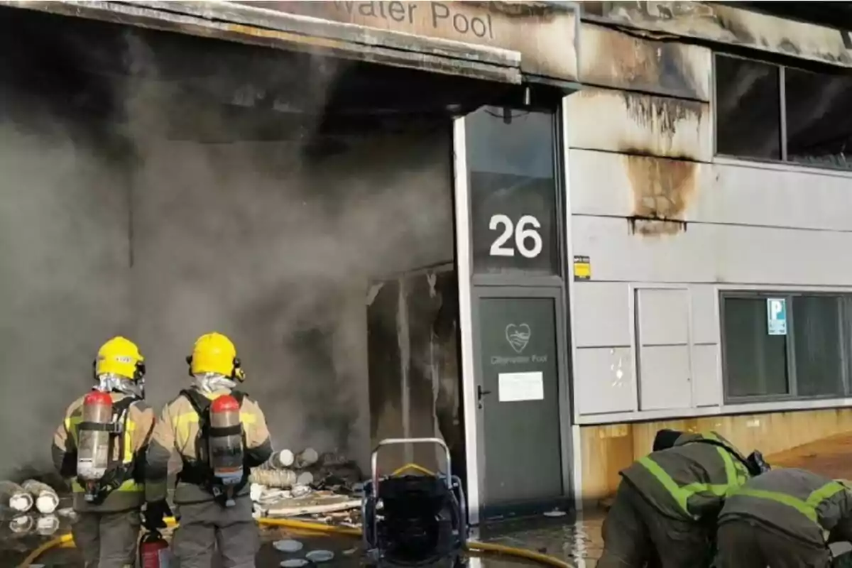 Bomberos trabajando para controlar un incendio en un edificio con humo saliendo por la puerta. Bomberos trabajando para controlar un incendio en un edificio con humo saliendo por la puerta.