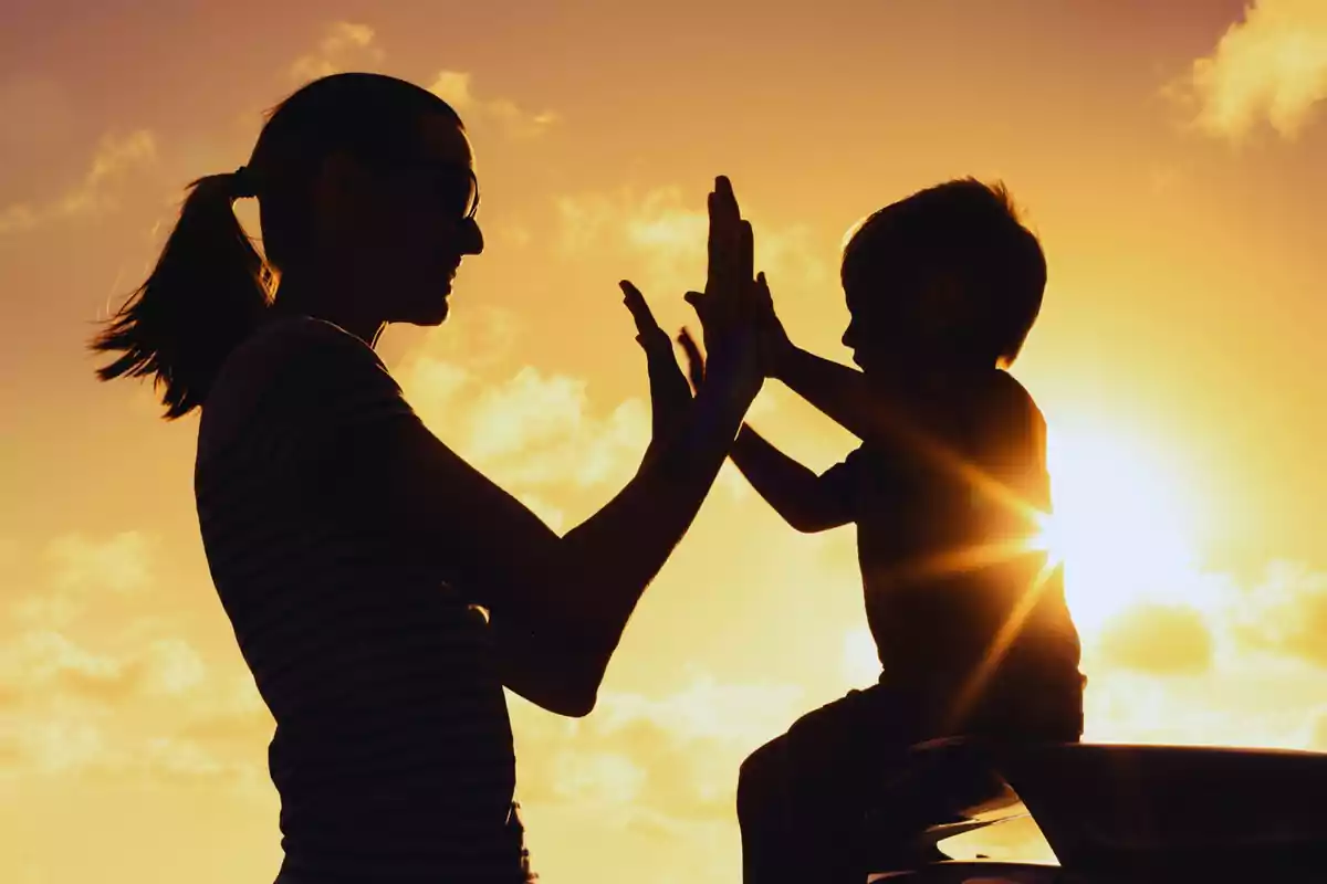 Silueta de una persona y un niño jugando al atardecer.