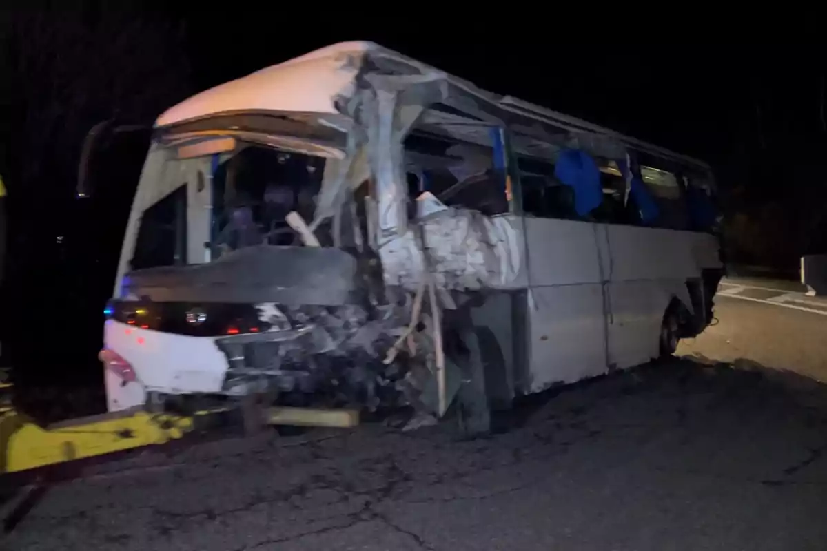 Un autobús blanc amb la part davantera malmesa en un accident nocturn.