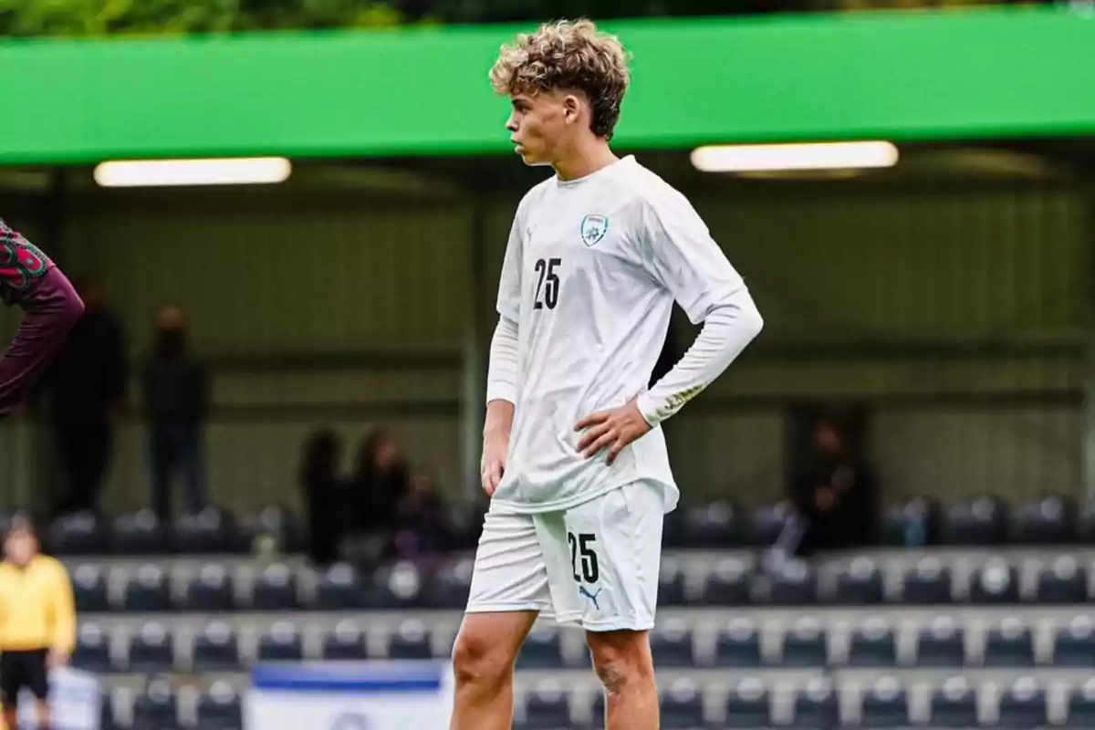 Un jugador de futbol amb l'uniforme blanc número 25 està dret al camp durant un partit.