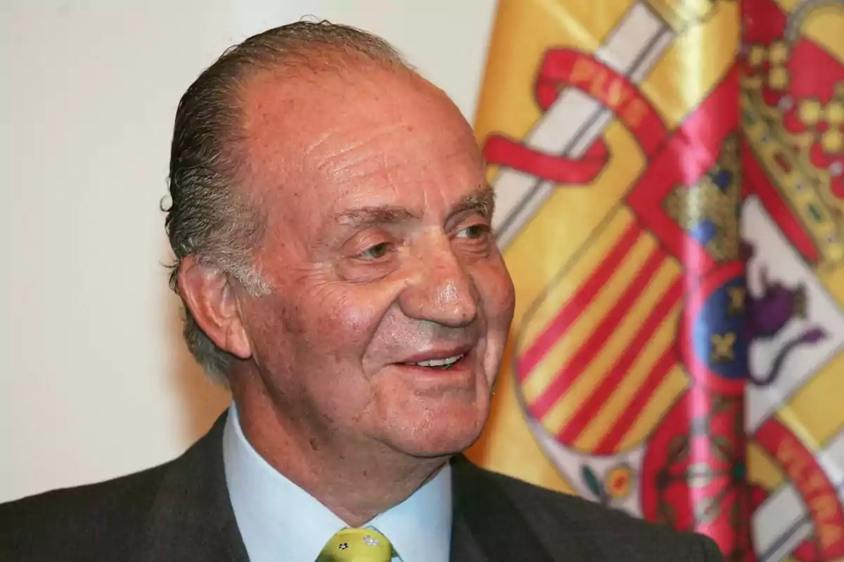 Un hombre mayor sonriendo con una bandera colorida de fondo.