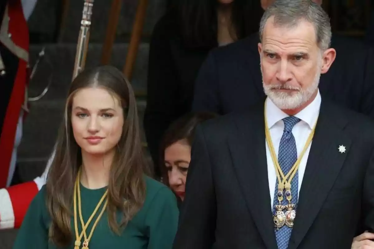 Dos personas vestidas formalmente con medallas alrededor del cuello en un evento oficial.