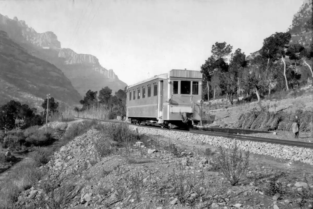 Un ferrocarril antic circula per una via envoltada de muntanyes i arbres