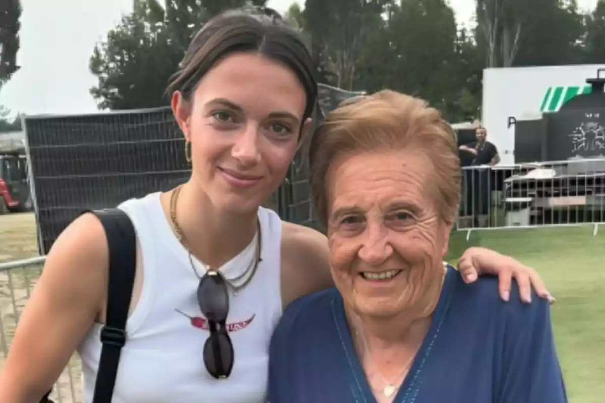 Dues dones somriuen abraçades a l’aire lliure en un esdeveniment, una jove amb samarreta blanca i una dona gran amb brusa blava Dues dones somriuen abraçades a l’aire lliure en un esdeveniment, una jove amb samarreta blanca i una dona gran amb brusa blava