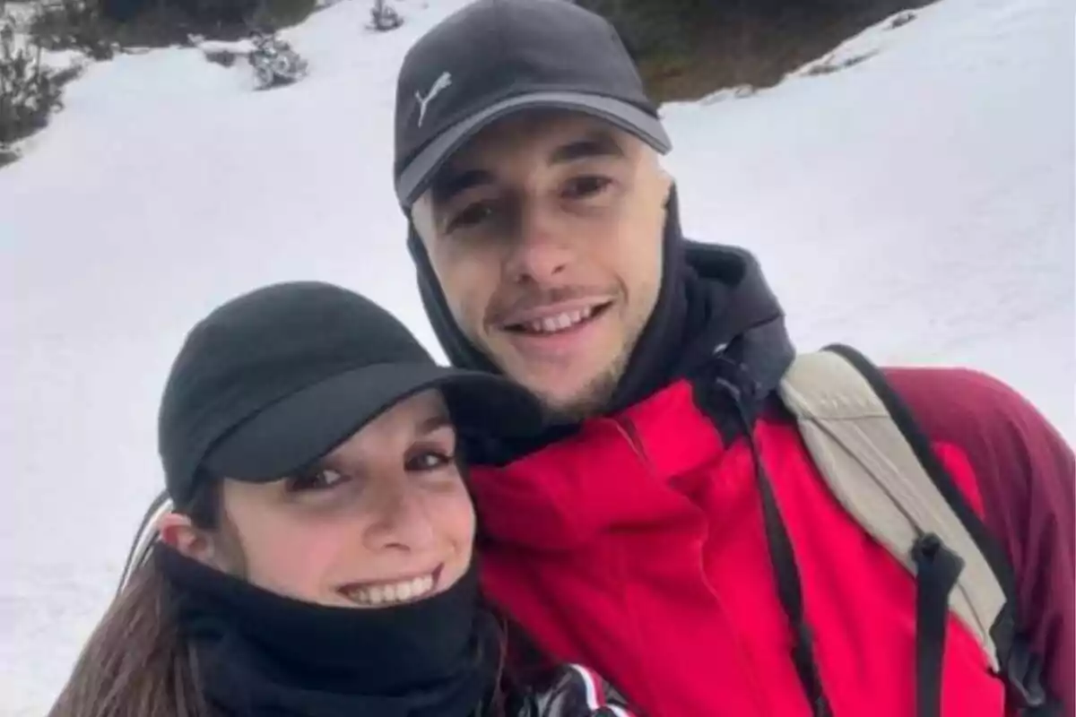 Parella jove somrient amb roba d’hivern i gorra negra en un paisatge nevat Parella jove somrient amb roba d’hivern i gorra negra en un paisatge nevat