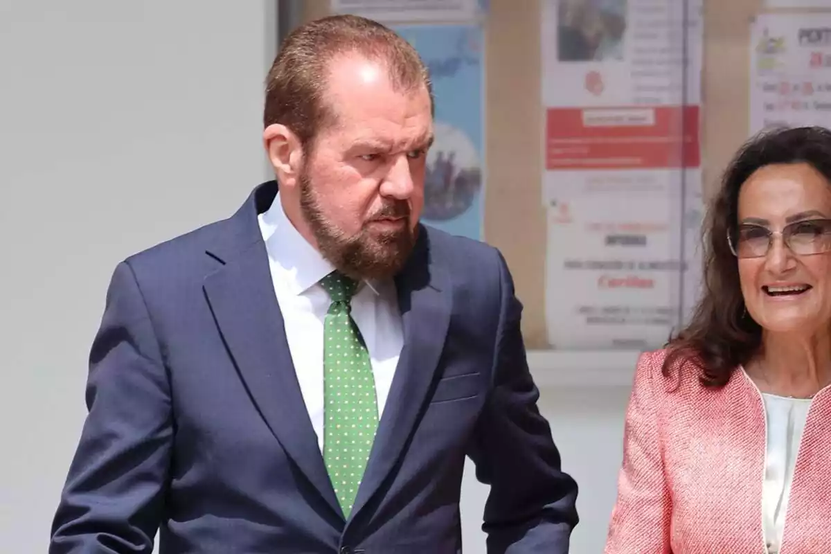 Foto de Jesús Ortiz caminant al carrer amb una dona, ell seriós i ella somrient, els dos vestits formalment Foto de Jesús Ortiz caminant al carrer amb una dona, ell seriós i ella somrient, els dos vestits formalment