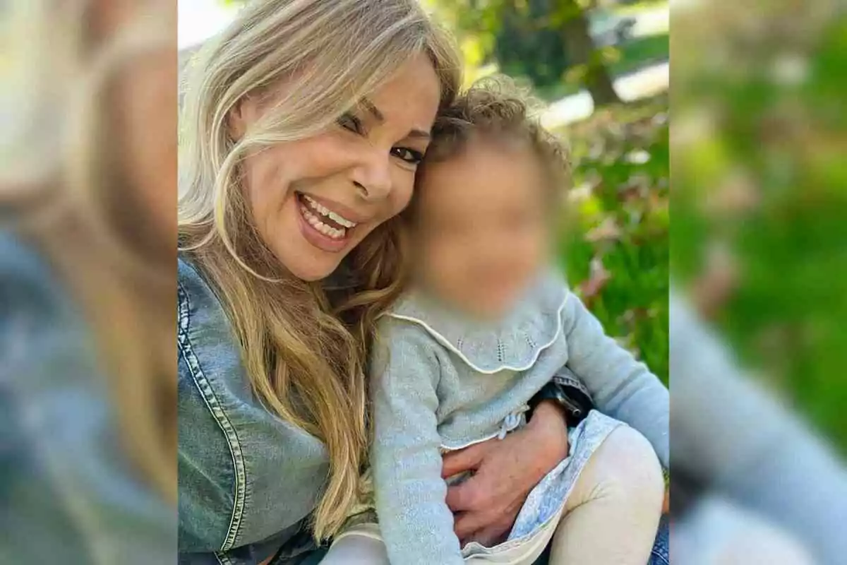 Ana Obregón somrient amb cabell ros abraça la seva neta Ana Sandra amb la cara difuminada en un parc. Ana Obregón somrient amb cabell ros abraça la seva neta Ana Sandra amb la cara difuminada en un parc.