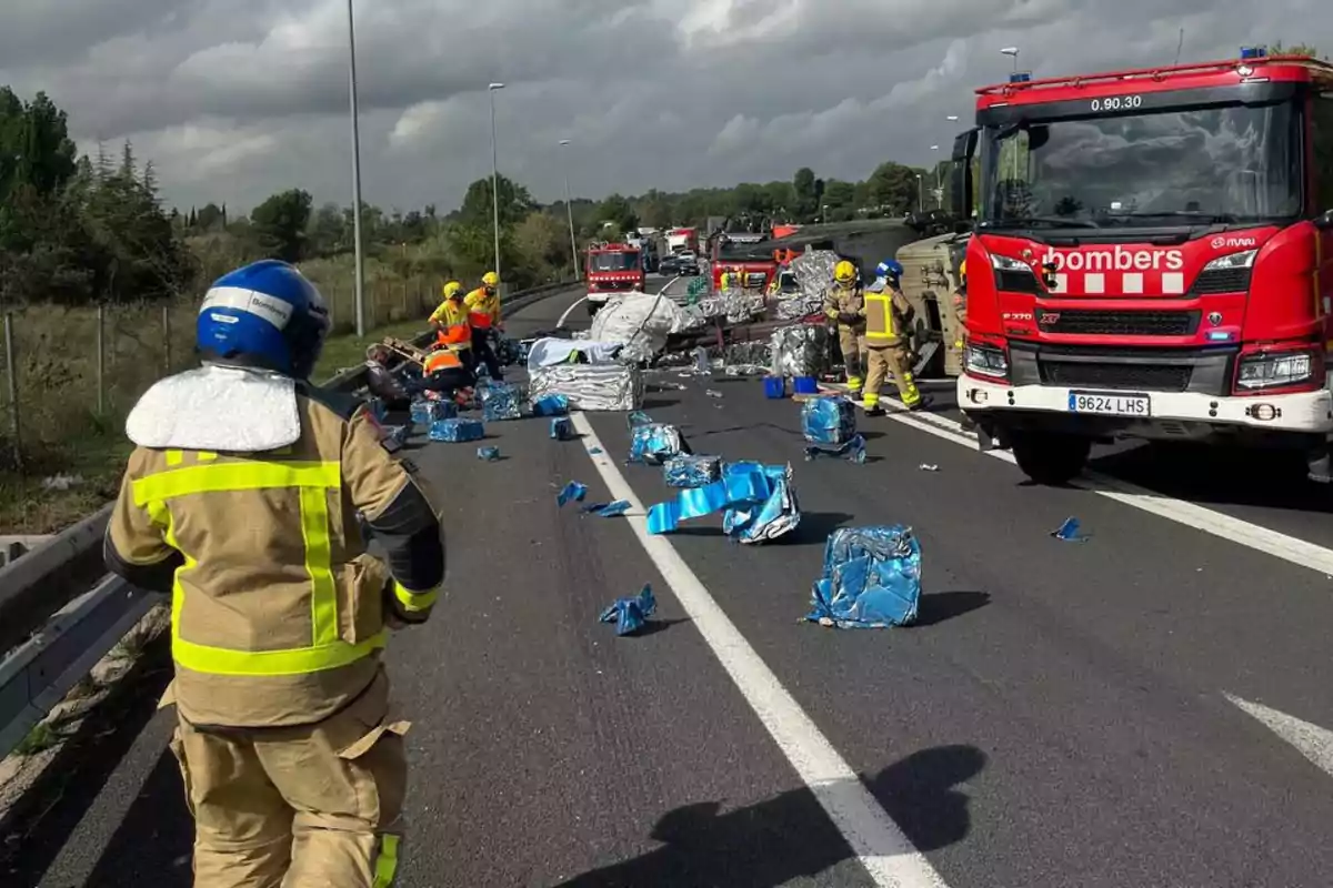 Bomberos trabajando en la escena de un accidente en la carretera con escombros esparcidos por el asfalto.