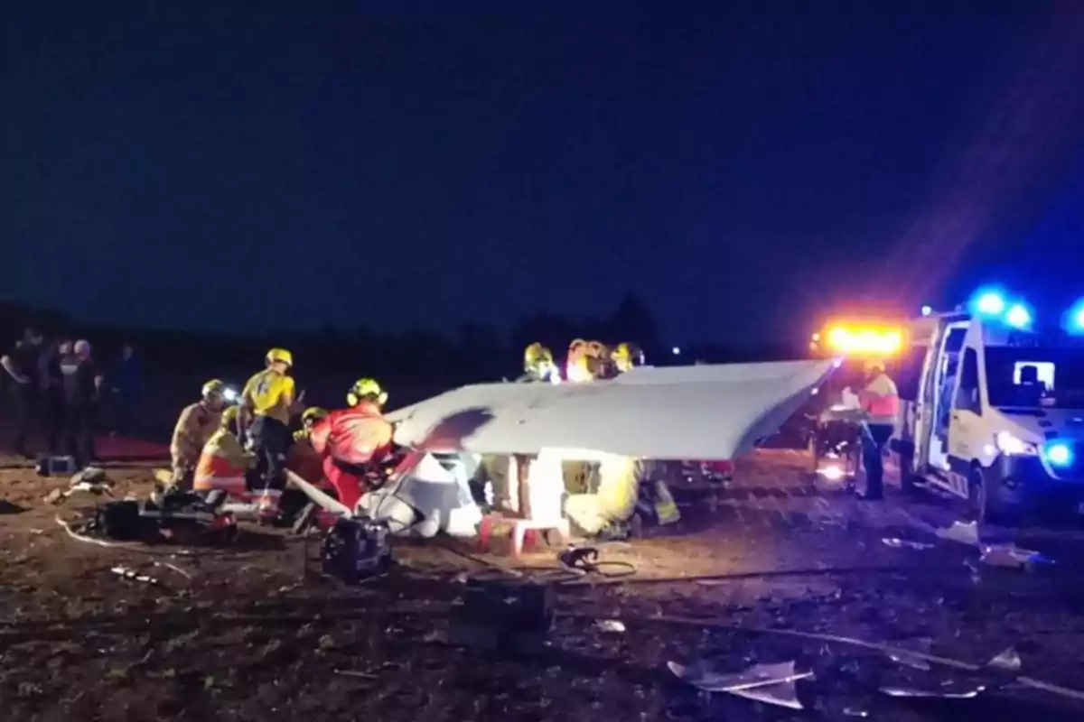 Un grup de rescatistes treballen al lloc d?un accident aeri durant la nit, amb llums d?emergència il·luminant l?escena.