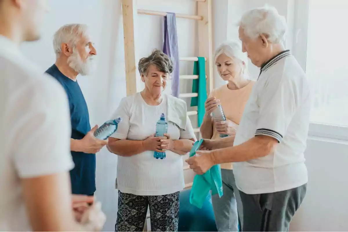 Un grup de persones grans sostenint ampolles d‟aigua mentre conversen en un entorn d‟exercici.