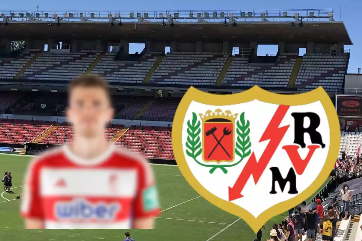 Un jugador de futbol desenfocat amb la samarreta del Rayo Vallecano i l?escut de l?equip en primer pla, amb un estadi de fons.