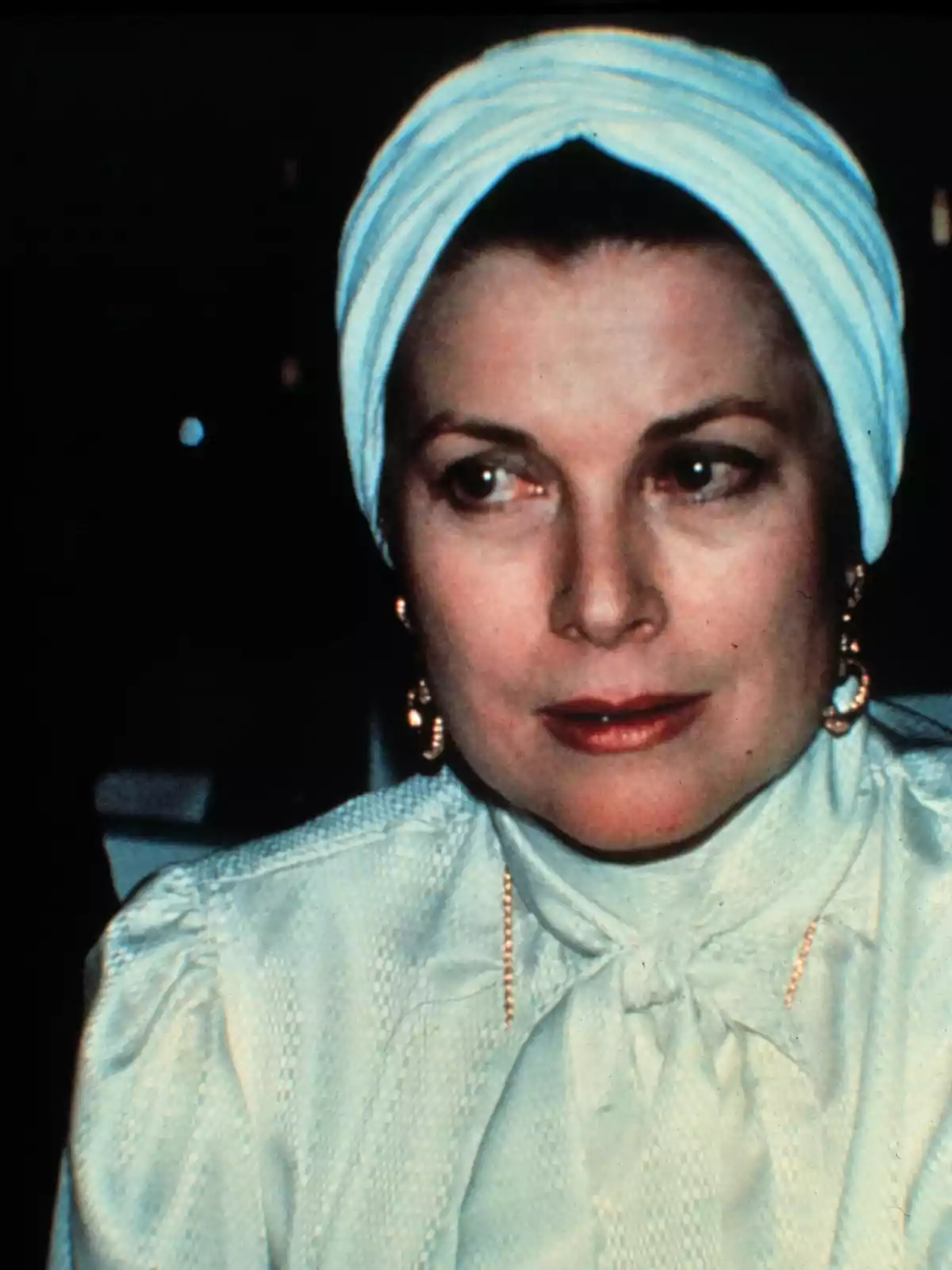 Grace Kelly con un turbante blanco y blusa clara mira hacia un lado.