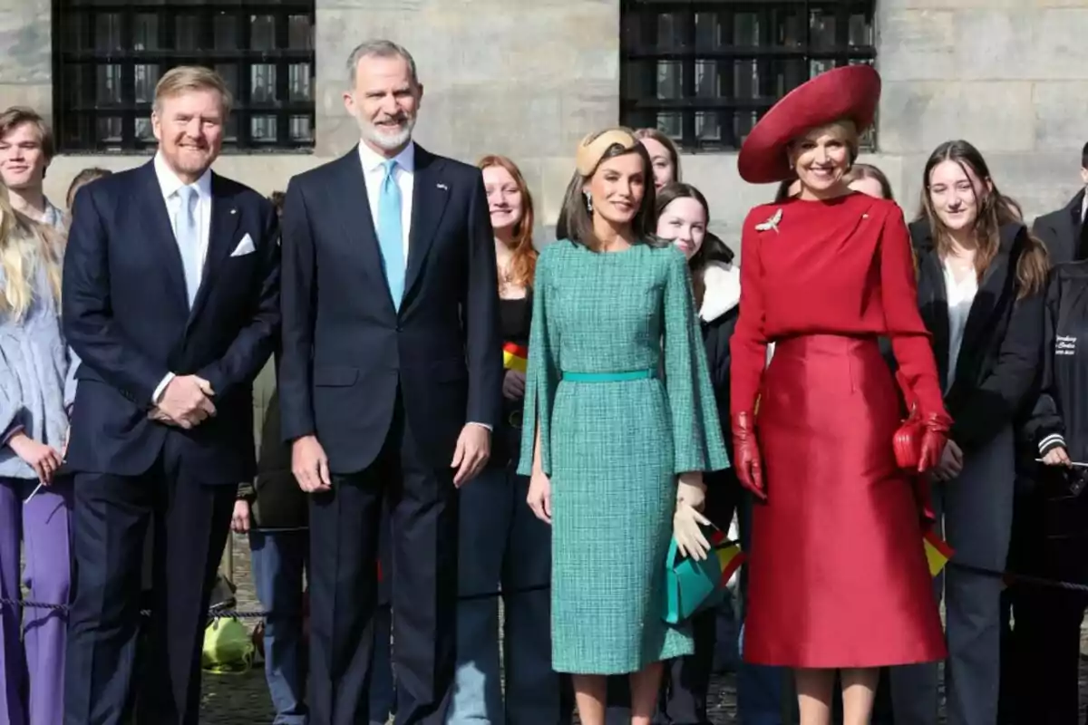 William of the Netherlands, Philip VI, Letizia and Máxima of Holland posing for a photo, all dressed elegantly, while several people in the background watch and smile. William of the Netherlands, Philip VI, Letizia and Máxima of Holland posing for a photo, all dressed elegantly, while several people in the background watch and smile.