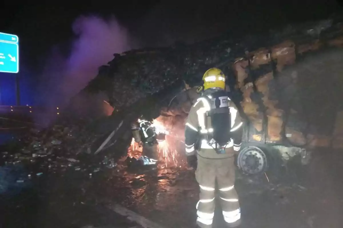 Bomberos trabajando en la escena de un accidente nocturno con un vehículo volcado y humo en el aire.