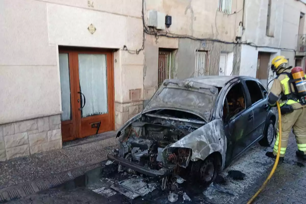 Un bomber apaga un cotxe cremat davant d?una casa en un carrer residencial.