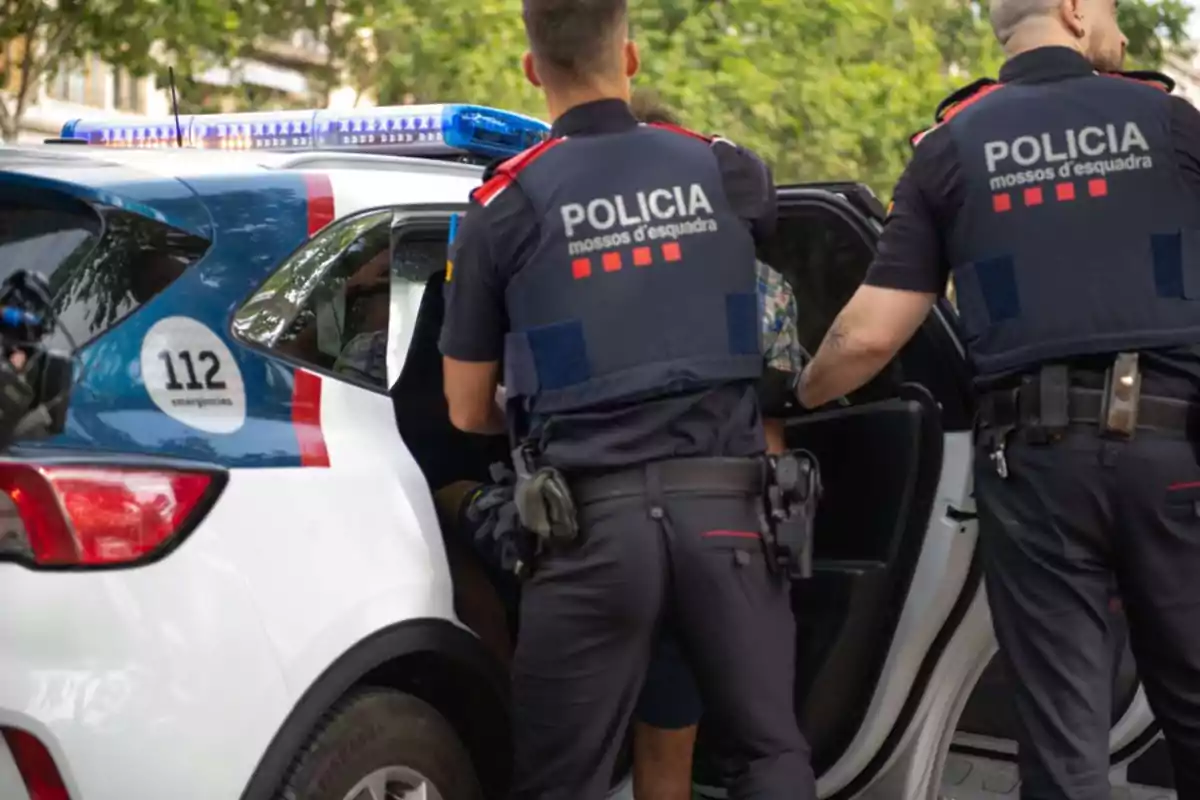 Dos agentes de policía introducen a una persona en un coche patrulla en un entorno urbano.