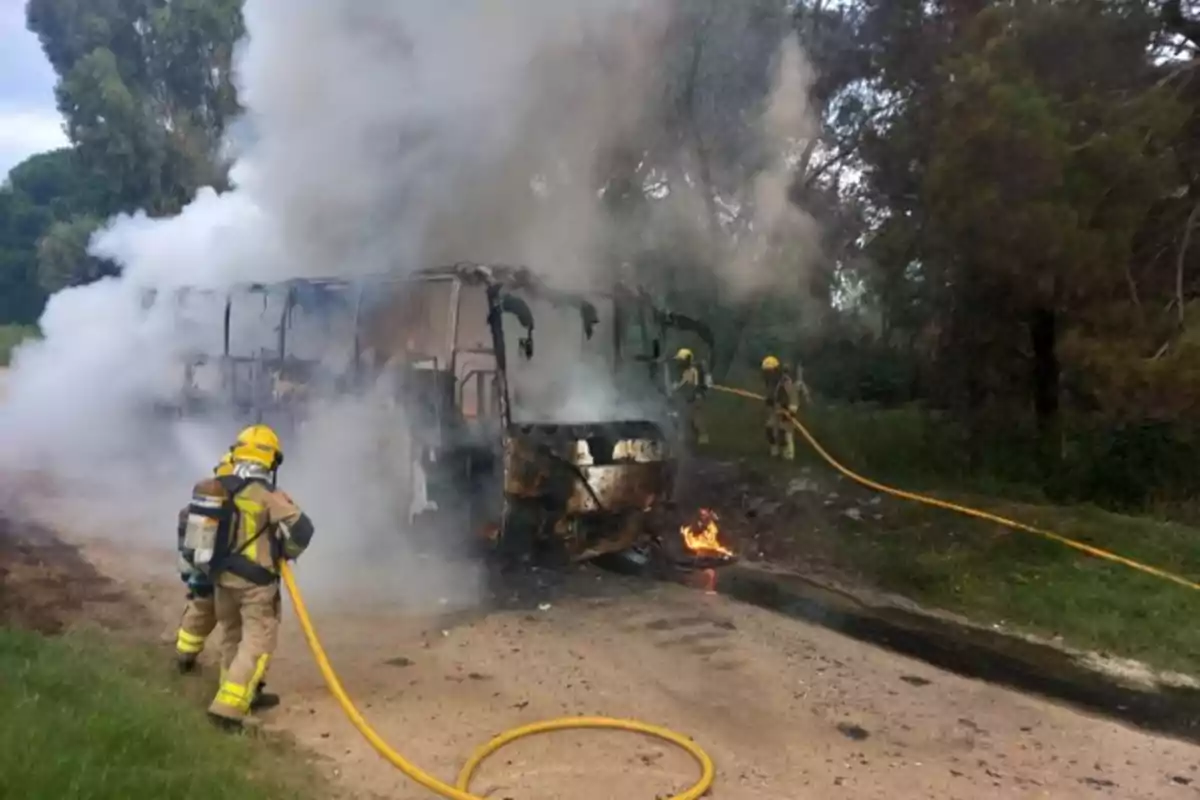 Bombers extingint un incendi en un autobús a una carretera envoltada d'arbres.