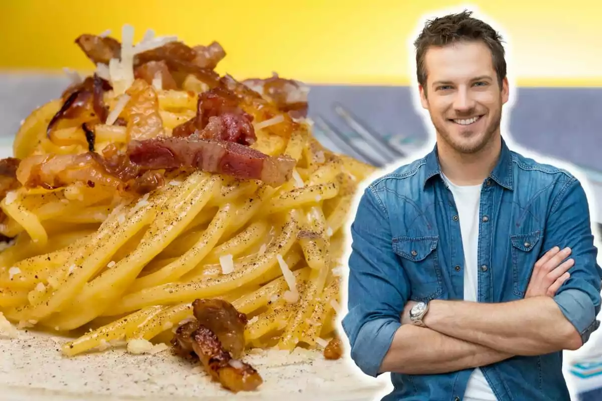 Un hombre sonriente con camisa de mezclilla está al lado de un plato de espagueti carbonara con trozos de tocino y queso rallado.