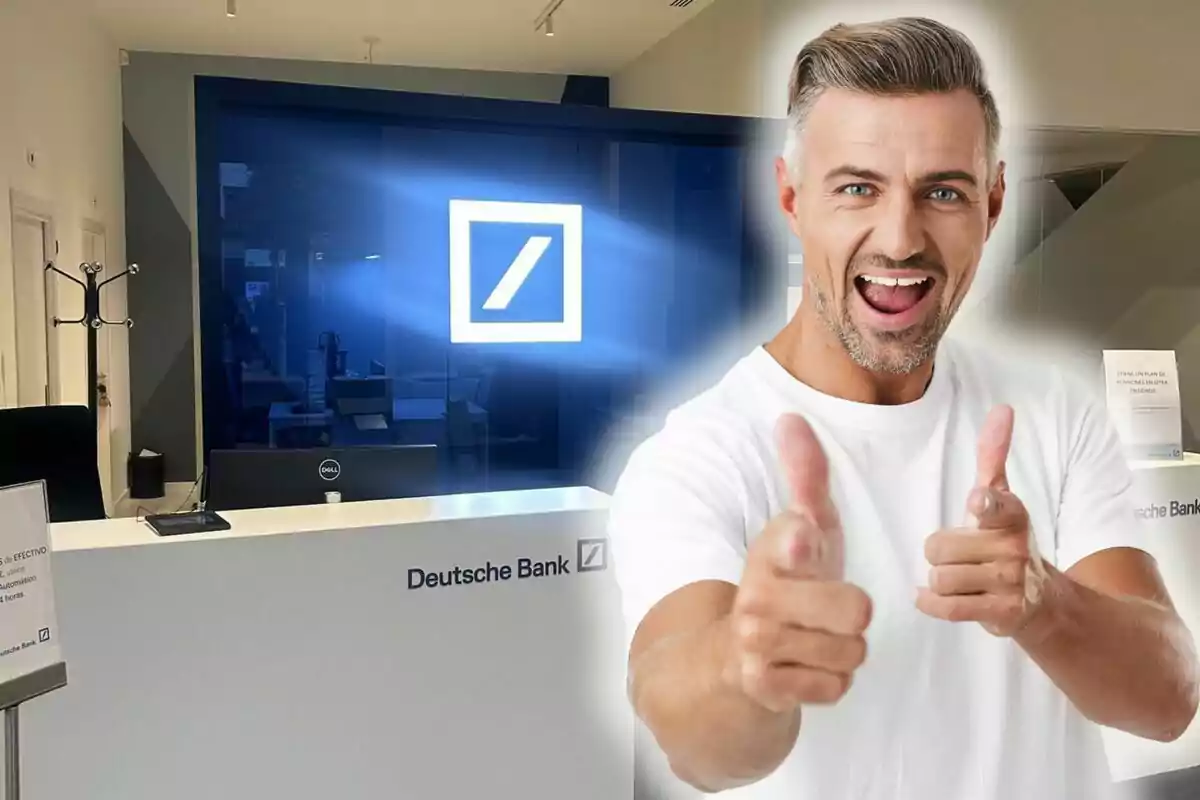 Un hombre sonriente con camiseta blanca hace un gesto de aprobación con ambas manos frente a un mostrador de Deutsche Bank.