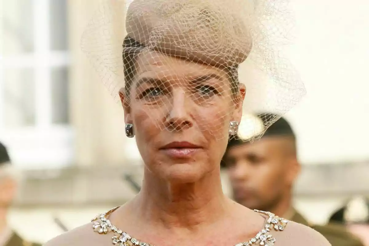 A person with an elegant beige hat adorned with a net and a dress with shiny details. A person with an elegant beige hat adorned with a net and a dress with shiny details.