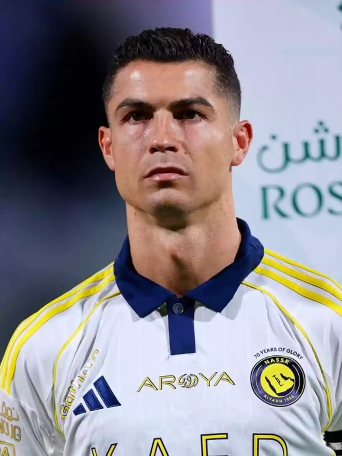 Soccer player wearing a white uniform with yellow details from a Saudi team looking forward during a sporting event Soccer player wearing a white uniform with yellow details from a Saudi team looking forward during a sporting event