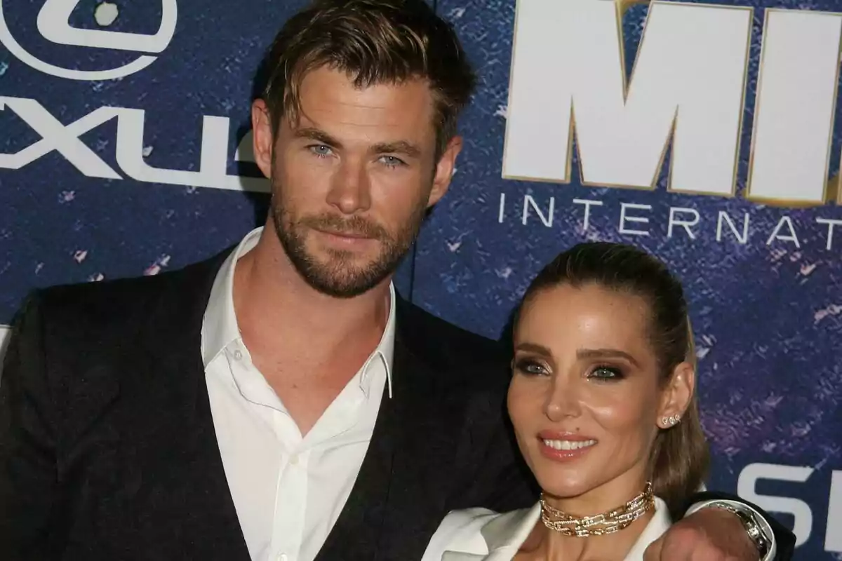 A couple, consisting of Elsa Pataky and Chris Hemsworth, posing together at an event with a blue background and white letters. A couple, consisting of Elsa Pataky and Chris Hemsworth, posing together at an event with a blue background and white letters.