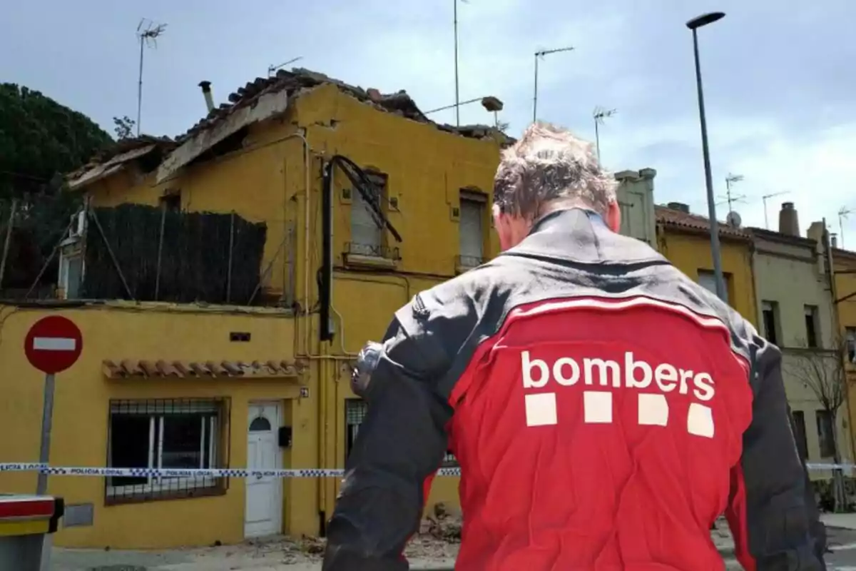 Un bomber d'esquena observa una casa groga amb el sostre danyat i acordonada per la policia local.