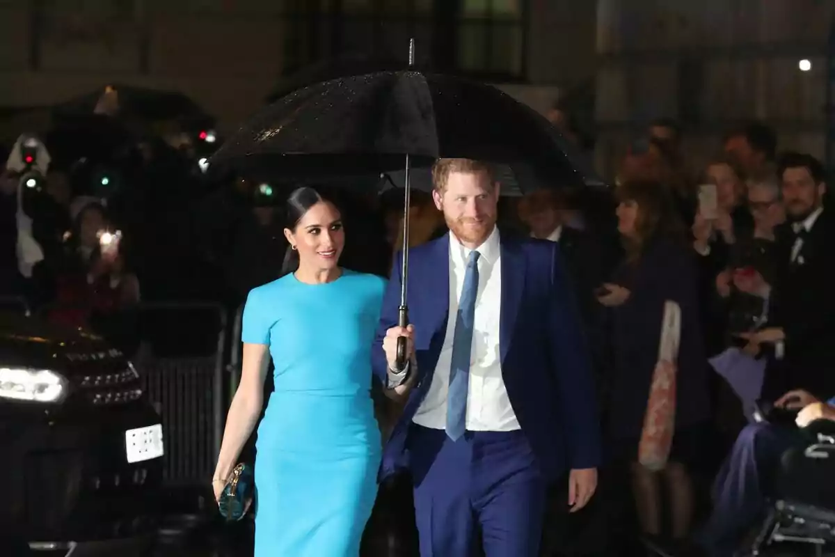Una parella elegant camina sota la pluja, compartint un paraigua negre mentre són fotografiats per una multitud de persones. Una parella elegant camina sota la pluja, compartint un paraigua negre mentre són fotografiats per una multitud de persones.