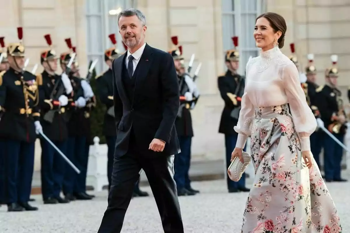 A smartly dressed couple walks past a group of uniformed guards at a formal event. A smartly dressed couple walks past a group of uniformed guards at a formal event.