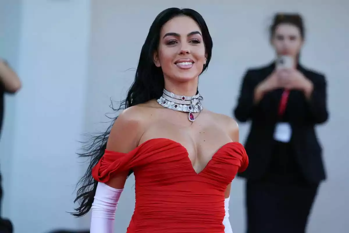 Dona amb vestit vermell elegant i guants blancs posant i somrient en un esdeveniment formal Dona amb vestit vermell elegant i guants blancs posant i somrient en un esdeveniment formal