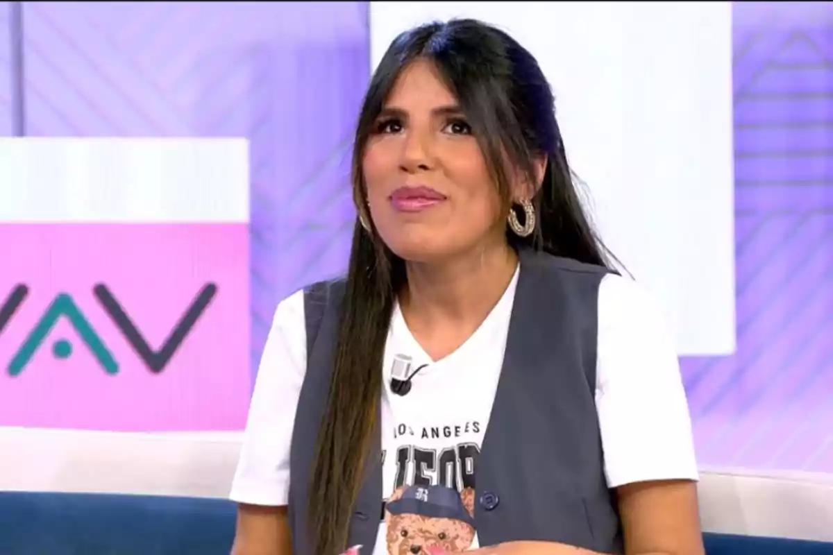 Isa Pantoja con cabello largo y oscuro está sentada en un set de televisión con fondo colorido, lleva una camiseta blanca con un diseño de oso y un chaleco gris, y está sonriendo mientras mira hacia arriba. Isa Pantoja con cabello largo y oscuro está sentada en un set de televisión con fondo colorido, lleva una camiseta blanca con un diseño de oso y un chaleco gris, y está sonriendo mientras mira hacia arriba.