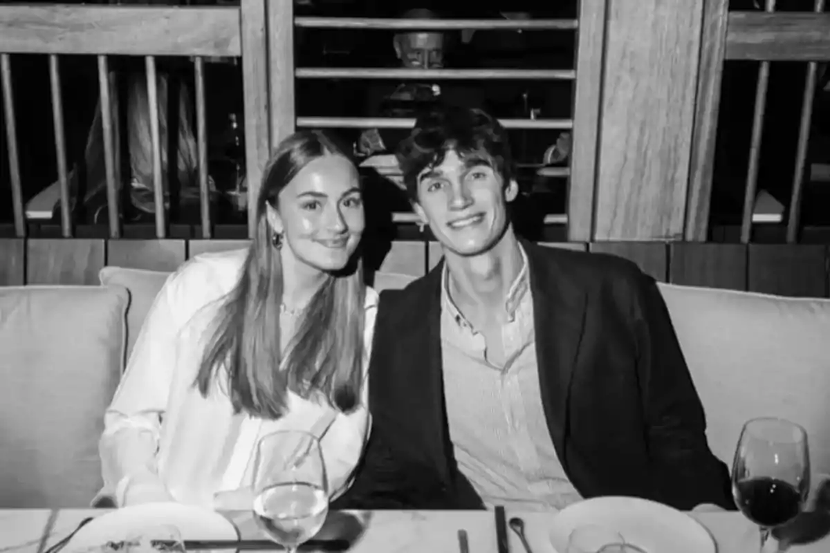 Una parella jove somriu mentre està asseguda en un restaurant elegant, amb copes de vi i plats a la taula. Una parella jove somriu mentre està asseguda en un restaurant elegant, amb copes de vi i plats a la taula.