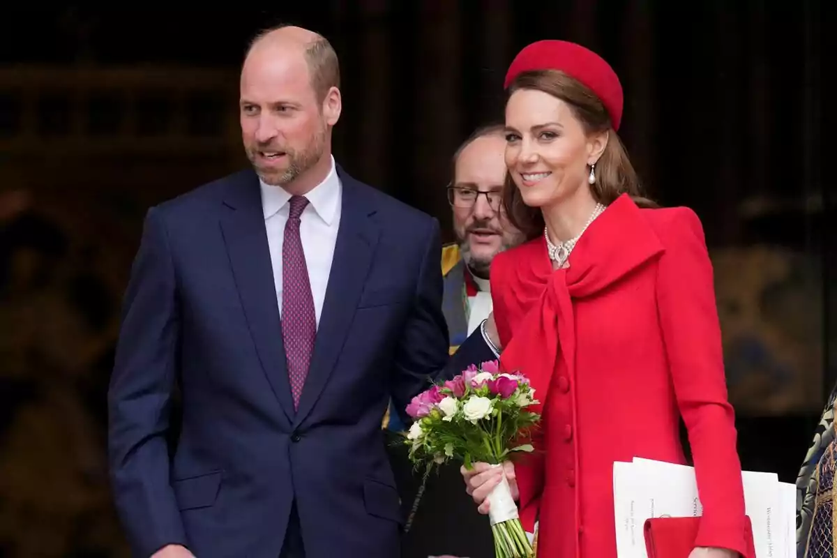 A smartly dressed couple exits a building, the woman carrying a bouquet of flowers and wearing a red outfit. A smartly dressed couple exits a building, the woman carrying a bouquet of flowers and wearing a red outfit.