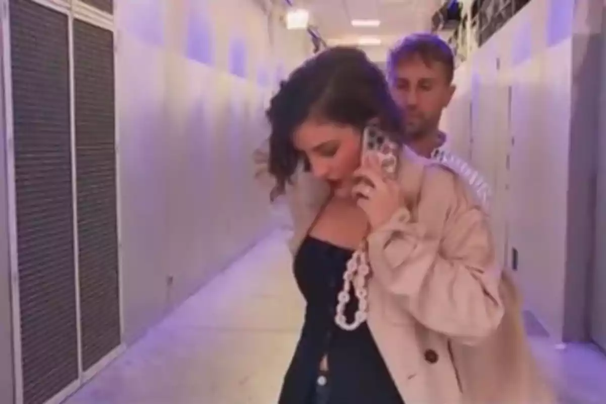 Una dona parlant per telèfon mentre camina per un passadís amb un home darrere d'ella. Una dona parlant per telèfon mentre camina per un passadís amb un home darrere d'ella.