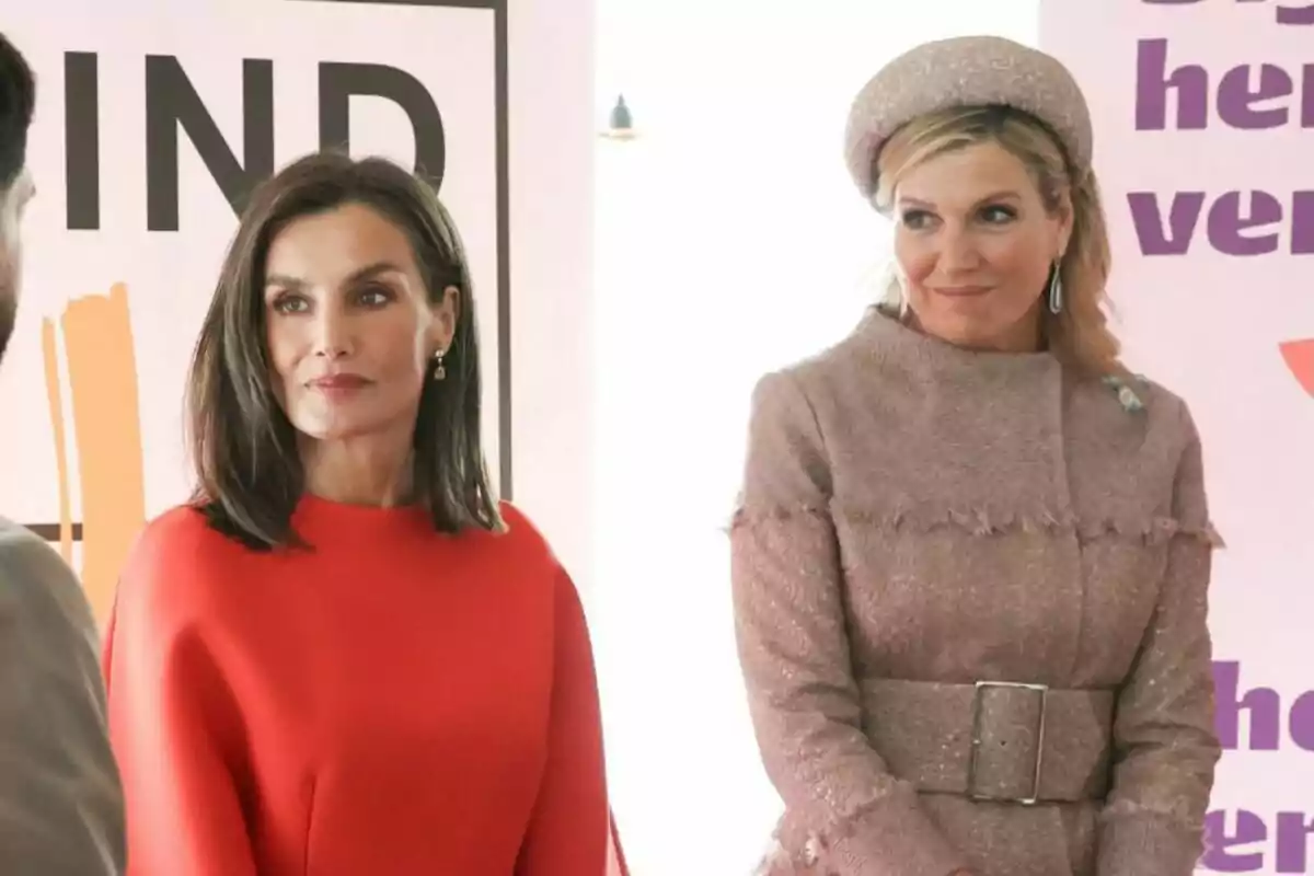Two elegantly dressed women, one in a red dress and the other in a beige outfit, pose together at an event.