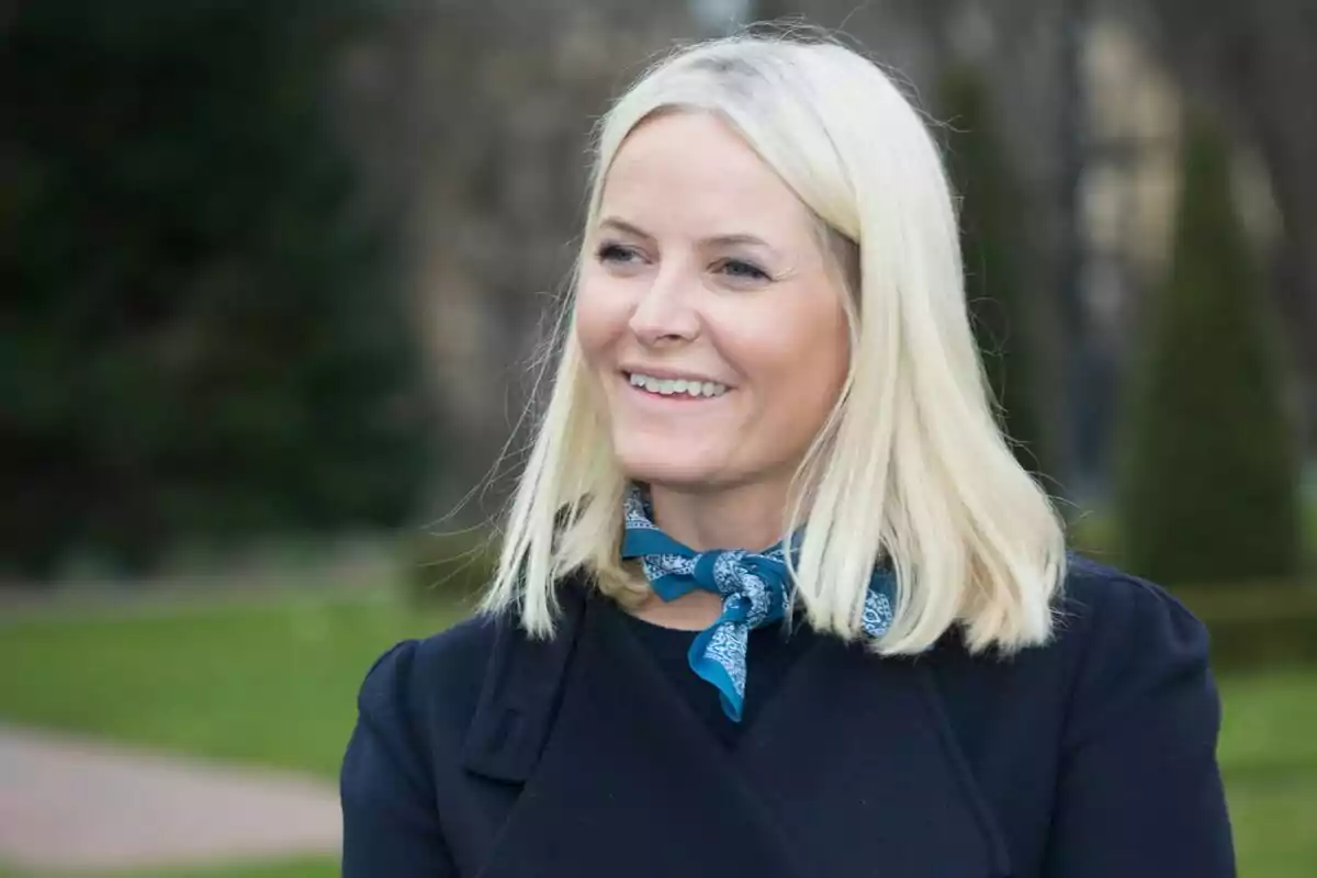 A blonde woman smiling outdoors with a blue scarf around her neck. A blonde woman smiling outdoors with a blue scarf around her neck.