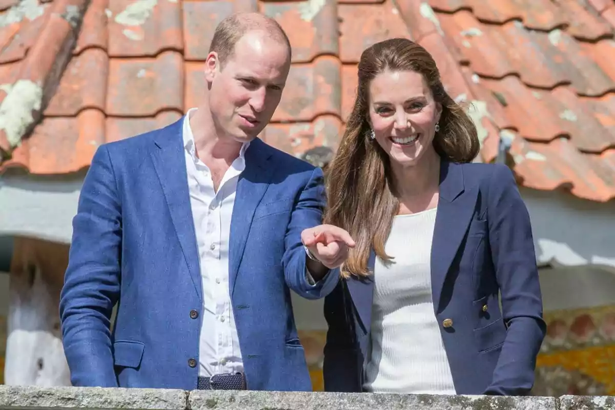 A smiling couple dressed elegantly in blue jackets posing in front of a tiled roof. A smiling couple dressed elegantly in blue jackets posing in front of a tiled roof.