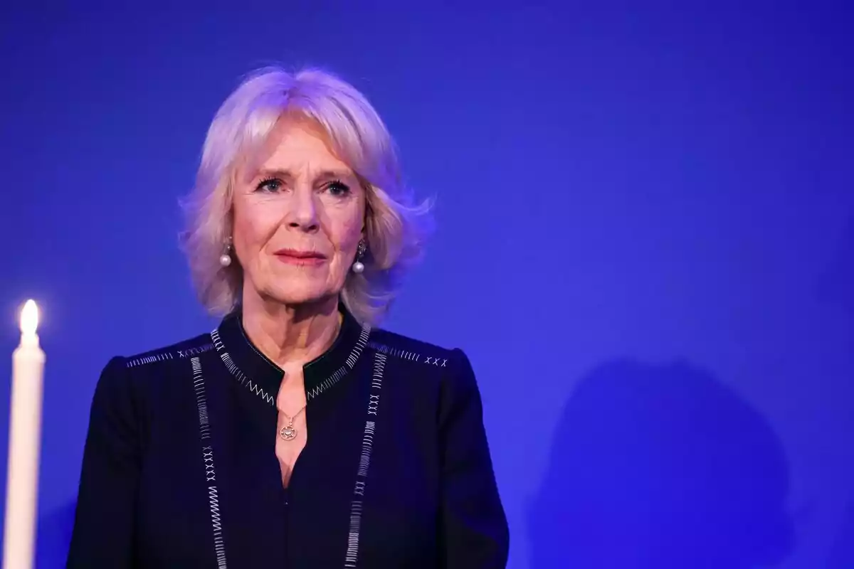 Dona de cabell ros i curt amb expressió seriosa vestida de negre davant d’un fons blau i una espelma encesa al seu costat Dona de cabell ros i curt amb expressió seriosa vestida de negre davant d’un fons blau i una espelma encesa al seu costat