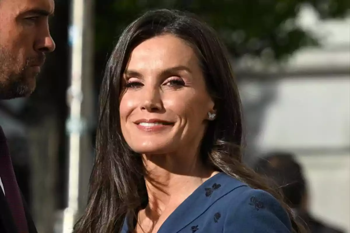 A smiling woman with long dark hair is wearing a blue dress with embroidered details and is outdoors. A smiling woman with long dark hair is wearing a blue dress with embroidered details and is outdoors.