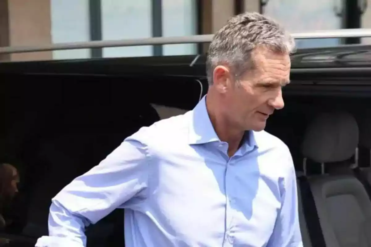 Hombre de cabello canoso con camisa azul claro saliendo de un vehículo negro.