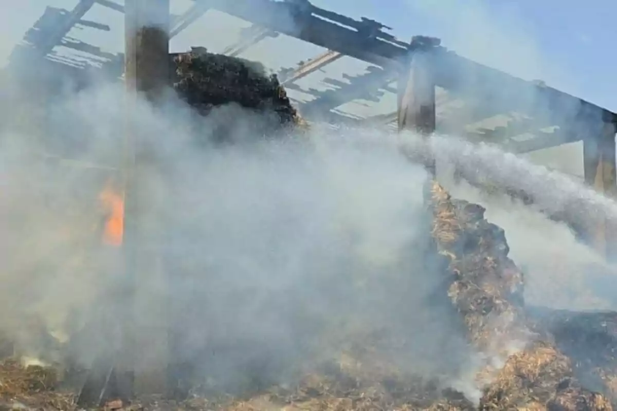 Un incendi en un estable de palla amb fum dens i aigua ruixada per apagar el foc