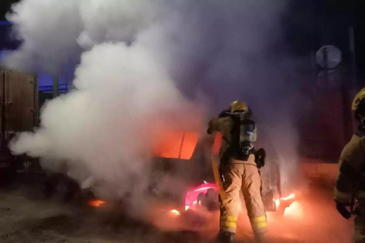 Bombers apagant un incendi en un vehicle amb fum dens al voltant.