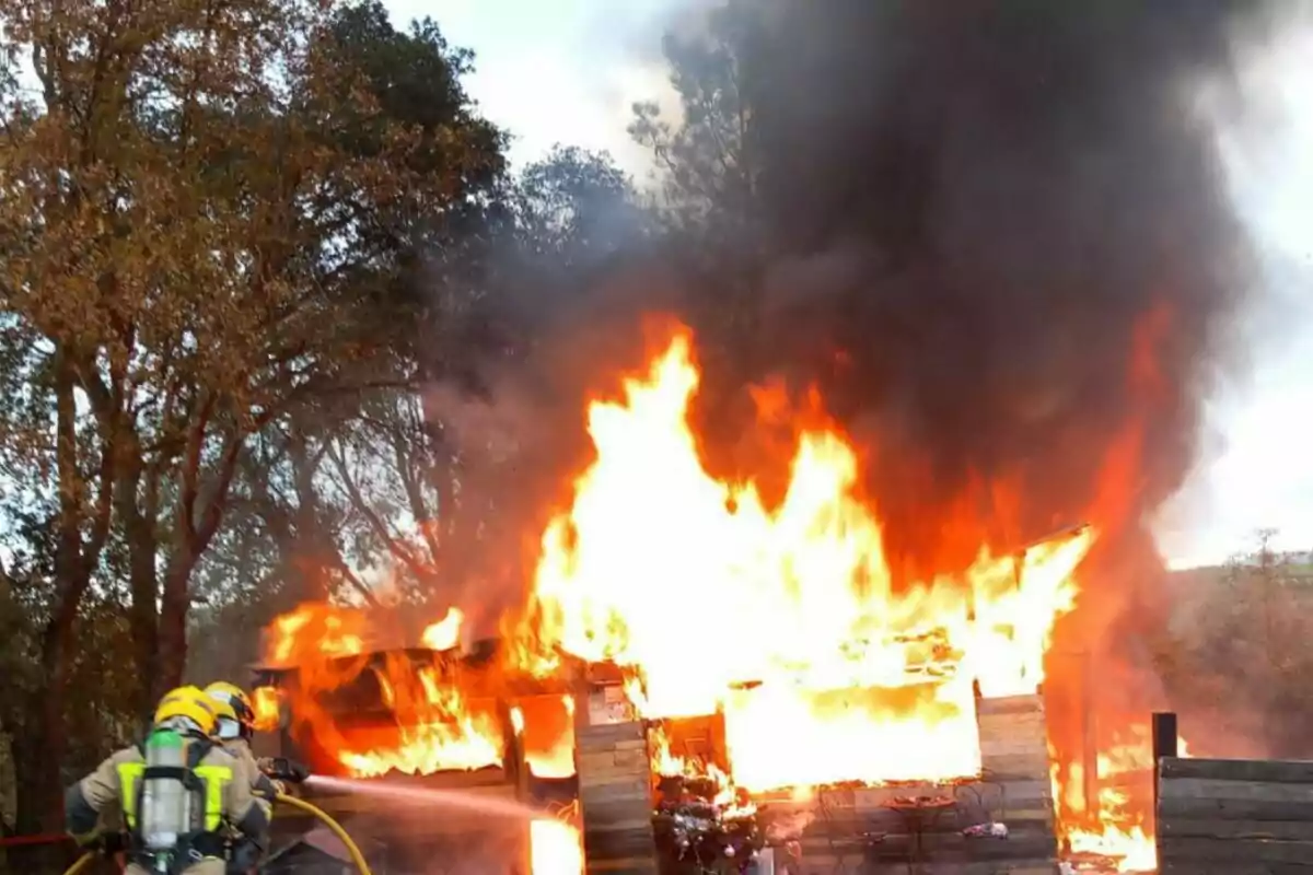 Bombers combatent un incendi en una estructura de fusta envoltada d'arbres.