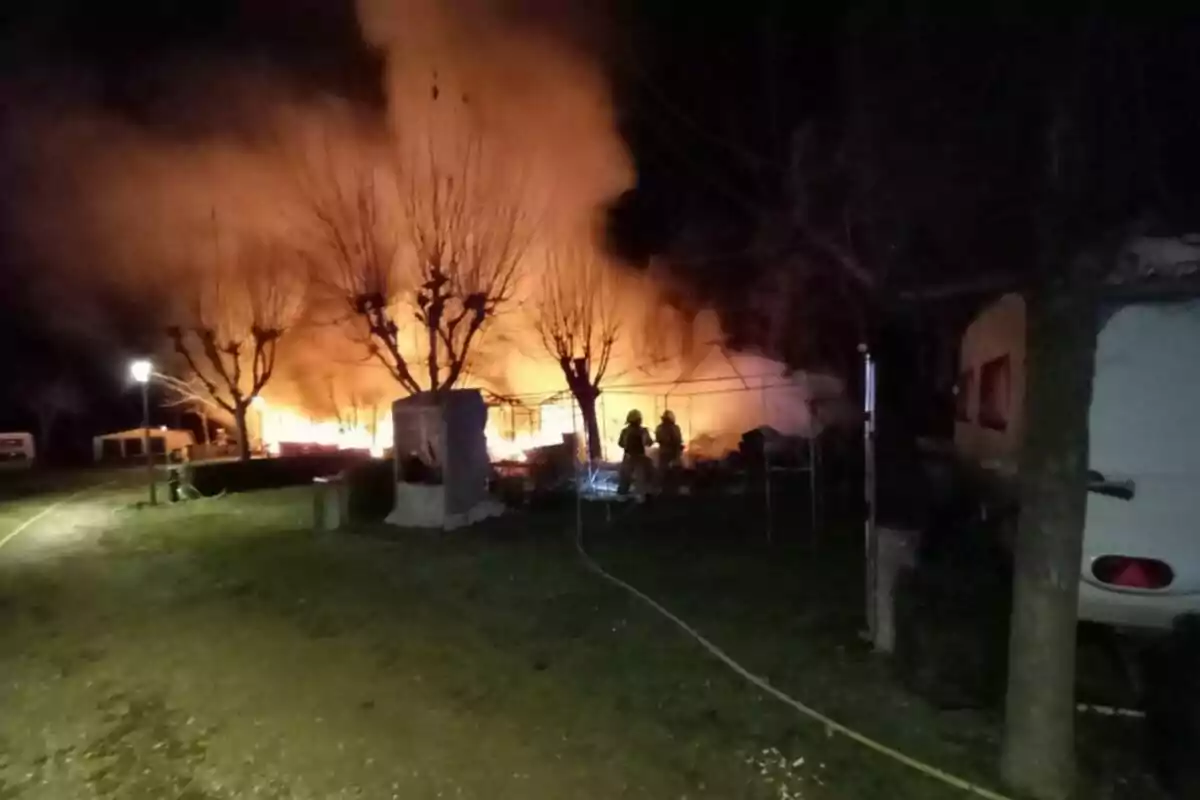 Incendi nocturn en una àrea arbrada amb bombers treballant al lloc.