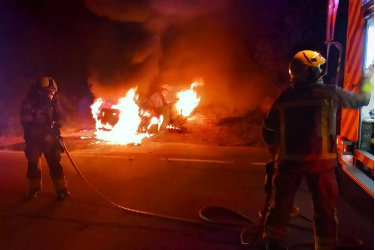 Bombers combatent un incendi d'un vehicle a la carretera durant la nit.