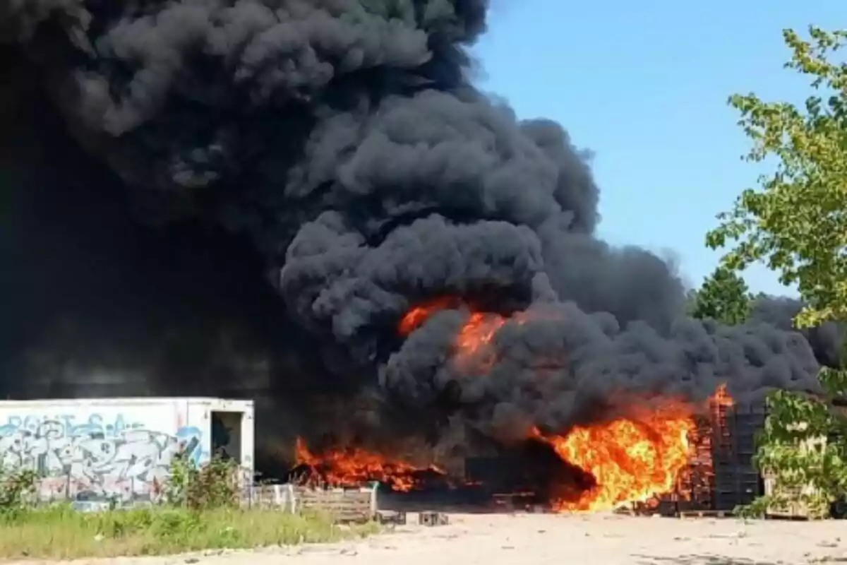 Incendi de gran magnitud amb flames intenses i fum negre en una zona industrial a l’aire lliure